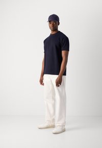 Marine blå strikket kortermet topp, hvite vide bukser, hvite sneakers og marineblå caps. Glatt tekstur, avslappet passform, moderne silhuett.