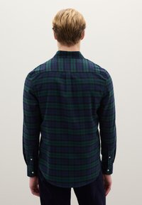 Lange mouw, geruit overhemd in donkere marineblauwe en groene tinten. Voorzien van een button-down kraag en afgeronde zoom, gemaakt van zachte, gestructureerde stof.