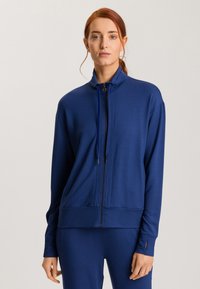 Chaqueta azul marino de cremallera fabricada en un tejido suave, con un cuello alto, mangas largas y bolsillos laterales. Presenta detalles de costura sutiles.