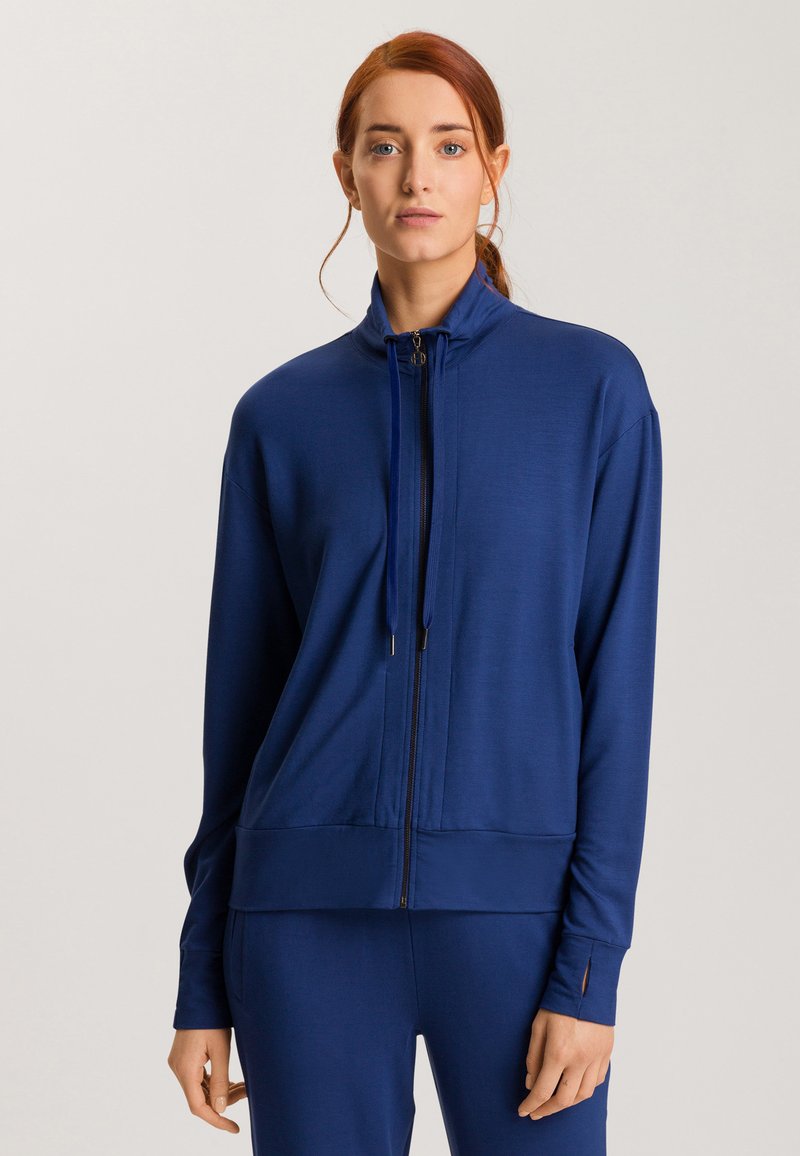 Chaqueta azul marino de cremallera fabricada en un tejido suave, con un cuello alto, mangas largas y bolsillos laterales. Presenta detalles de costura sutiles.