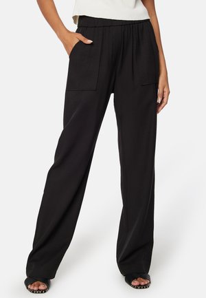 Pantaloni larghi neri con cintura elastica, due grandi tasche laterali, texture del tessuto liscia e design fluido.