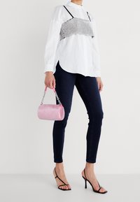 Camisa blanca de botones, top corto a cuadros en blanco y negro, jeans ajustados oscuros, tacones negros y una bolsa cilíndrica brillante de color rosa.