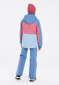 Bunte Skijacke in Hellblau, Pink und Dunkelblau, mit Kapuze, elastischen Bündchen und Schneehosen. Strukturierte, gestrickte pinke Mütze.