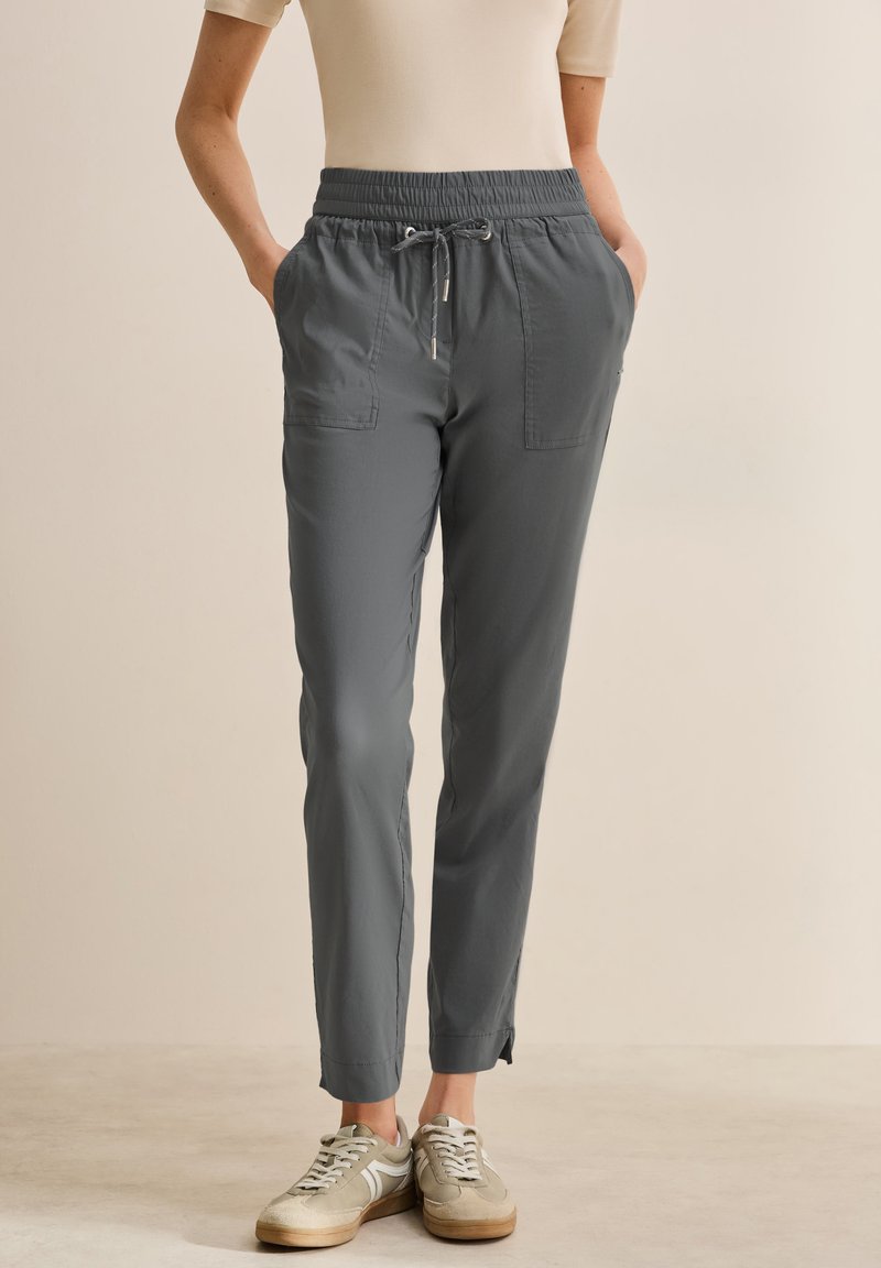 Pantalons légers gris avec une taille élastique, cordon de serrage, deux poches latérales, jambes fuselées et détails discrets au niveau de l'ourlet.
