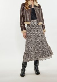 Brązowa skórzana krótka kurtka z kremowym kołnierzem i mankietami z sztucznego futra, zestawiona z czarną, kwiecistą, warstwową midi spódnicą. Czarne kozaki za kolano.