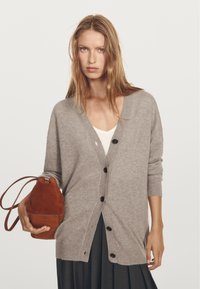 Grå ullkofta med V-ringning, långa ärmar och svarta knappar, kombinerad med en rostfärgad mocka-bucket bag. Vit topp under.