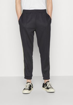 Ciemnoszare dresy o dopasowanym kroju, z elastycznym pasem, bocznymi kieszeniami i żółtymi paskami po bokach. Zestawione z czarno-białymi sneakersami.