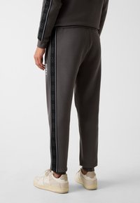 Grau melierte Jogginghose mit schwarzen Seitstreifen, die ein Logo-Muster und Text zeigen. Weiches Material, taillierte Passform mit einem gerippten Bund.