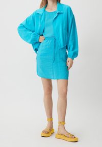 Veste bleu clair avec des poignets élastiques, associée à une robe assortie dotée d'une taille à cordon. Des sandales à plateforme jaunes complètent la tenue.