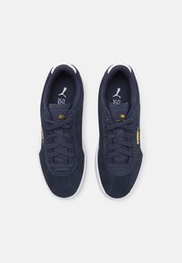 Marineblå ruskinnssneakers med hvite gummisåler, med flate lisser, gull Puma-logo og polstret krage for komfort.