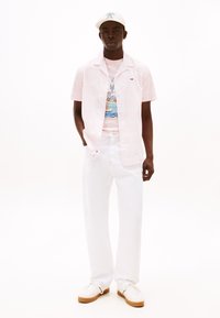 Camicetta rosa a maniche corte con un motivo sottile, abbinata a una leggera t-shirt grafica, pantaloni bianchi e sneakers bianche con suola beige.