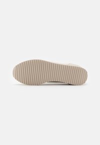 Sole of beige sneaker with a ridged, ribbed pattern running horizontally across the entire bottom surface.