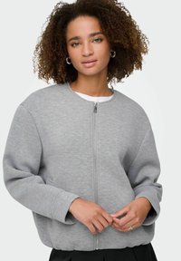 Sweatshirt zippé gris avec col rond, coupe oversize, poignets côtelés et poches. Fabriqué en tissu doux et texturé.