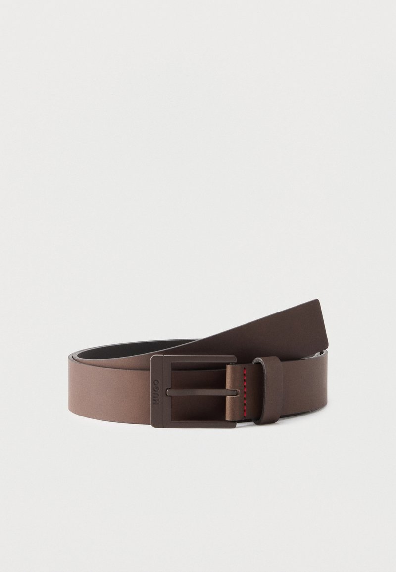 Ceinture en cuir marron avec une boucle rectangulaire en métal foncé mat, partiellement enroulée sur un fond blanc uni.