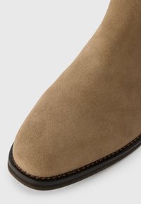 Soe nahk saapad heledas pruunis, sileda tekstuuriga, ruudukujulise varbaga ning tumeda tallaga, millel on kontrastsed õmblused.