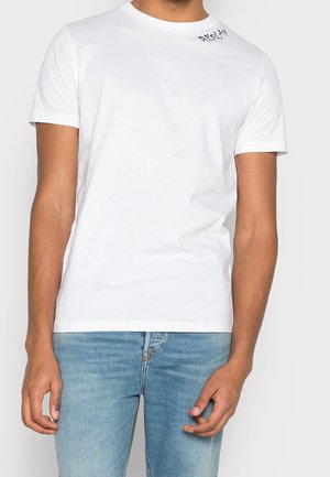 Mężczyzna w prostym, białym, krótkim rękawie z małym czarnym napisem "REPLAY" blisko kołnierza, w połączeniu z jasnoniebieskimi dżinsami.