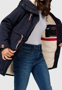 Granatowa kurtka z miękką białą podszewką, z brązowymi skórzanymi akcentami i zamkiem błyskawicznym. Wnętrze z kieszeniami do organizacji.