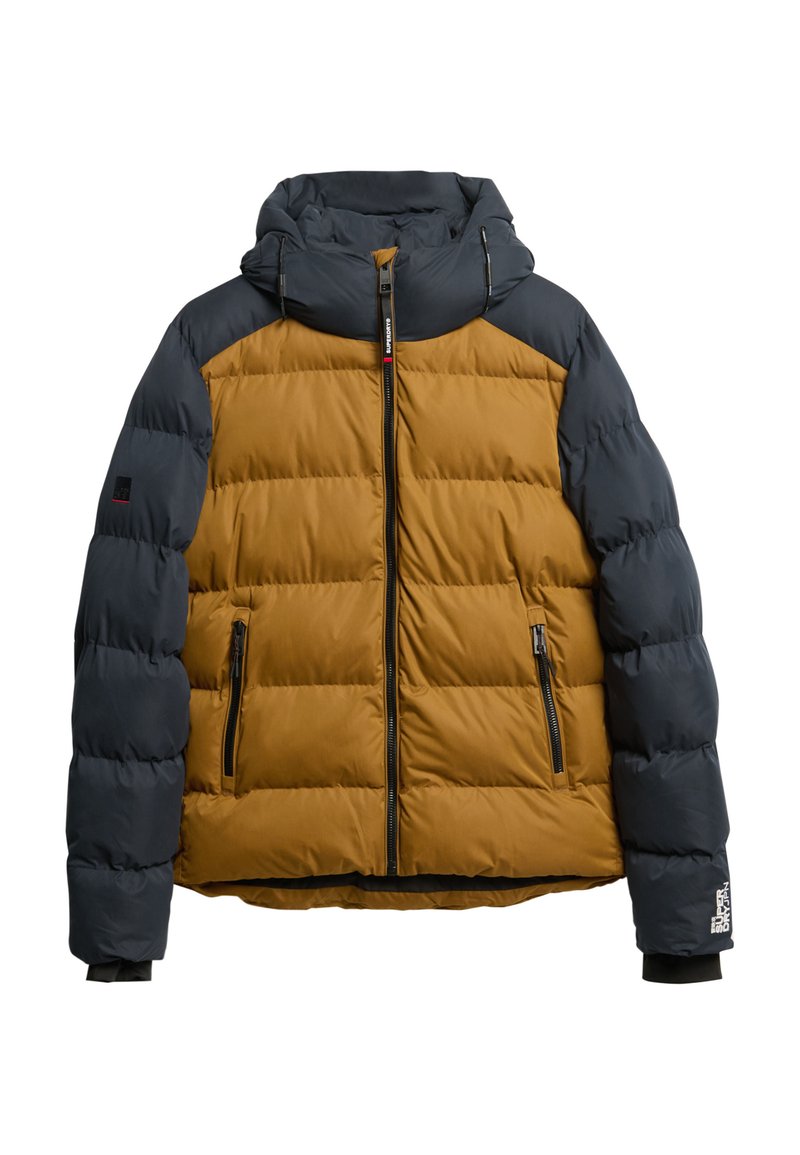 La giacca a vento presenta un corpo marrone con maniche blu navy, un cappuccio, imbottitura orizzontale, chiusura con zip e dettagli neri su polsini e tasche.