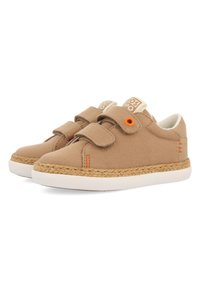 Zapatillas de lona beige con correas de velcro, suelas de goma blanca y detalles de yute alrededor de la suela. Presentan un acento naranja y un logo en la lengüeta.