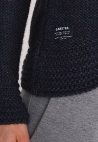 Navyblauer gestrickter Pullover mit strukturierter Oberfläche, versehen mit einem Etikett "Gaastra International Water Gear". Enthält ein weißes Innenfutter.