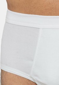 Slip in cotone bianco a costine con cinturino elastico, caratterizzati da una superficie liscia e un leggero lucido. Dettagliati con una sottile cucitura laterale.