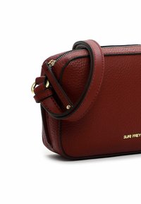 Borsa a tracolla rossa in pelle con superficie texture, dettagli neri, chiusura con zip e tracolla removibile. Logo dorato stampato sul davanti.