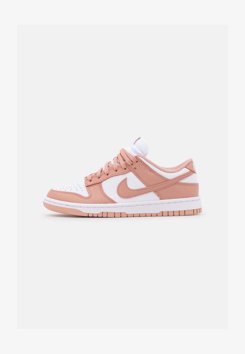 Tenisice s bijelim kožnim vrhom, svijetloružičastim kožnim detaljima i teksturiranom ružičastom i bijelom potplatu. Imaju vezice i Nike logo.