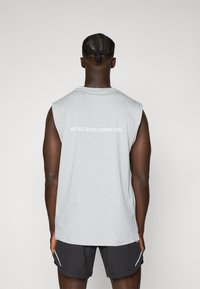 Grå ermeløs t-skjorte med hvit teksttrykk "NEVER STOP COMPETING" på ryggen, laget av myk stoff med en avslappet passform.