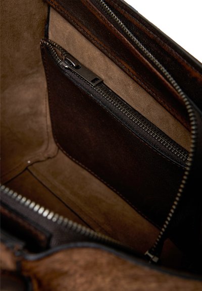 Intérieur d'un sac en cuir brun avec une poche zippée, texture lisse et doublure en daim contrastante dans des teintes plus claires et plus foncées.