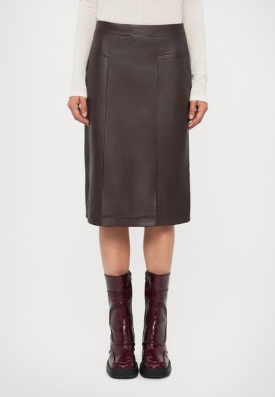 Woman wearing a knee-length dark brown leather skirt with front pockets and shiny burgundy mid-calf boots with black soles.