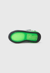 Sneakerzool met een zwart getextureerd rubberen buitenkant, felgroene doorschijnende demping en cirkelvormige luchtbeldetails aan de onderzijde.