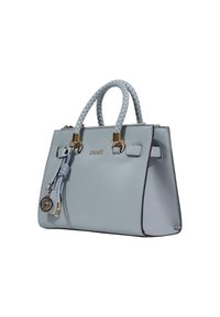 Lyseblå læderhåndtaske med en struktureret form, flettede håndtag, gyldent hardware og en dekorativ kvast. Har en logo på forsiden.