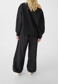 Zwarte oversized sweatshirt met een brede halslijn en lange mouwen, gecombineerd met bijpassende wijde broek, beide gemaakt van een zachte stof.