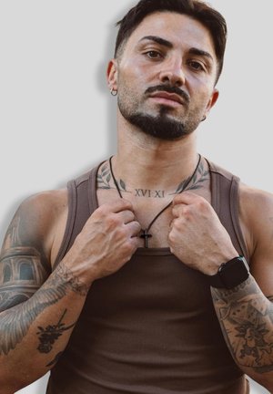 Braunes geripptes Tanktop, tätowierte Arme, schwarze Kreuzkette und Smartwatch. Auffällige Tattoos auf den Armen und im Schulterbereich.