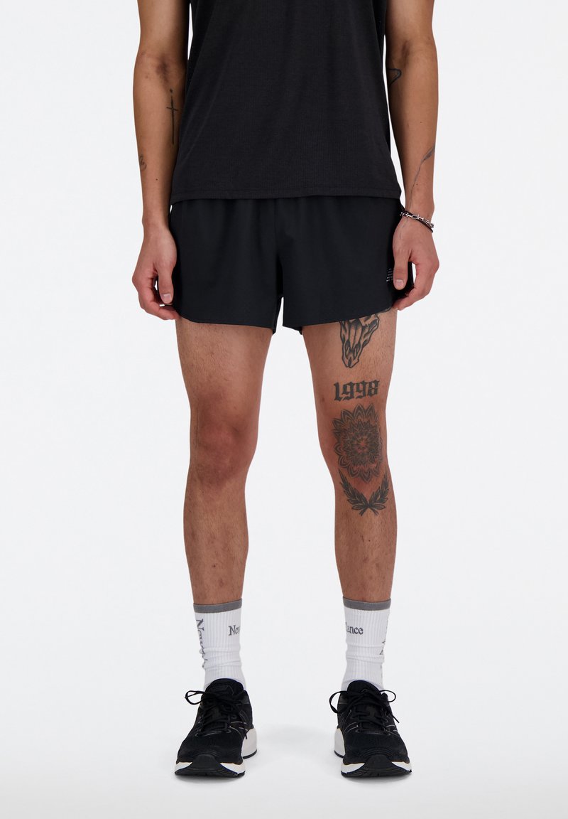 Shorts de sport noirs avec une coupe décontractée, associés à un t-shirt noir et des baskets noires. Tatouages notables sur les jambes inférieures.