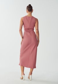 Mauve midi dress with a fitted waist, sleeveless design, and smooth texture. Features a back tie detail and subtle side slit.