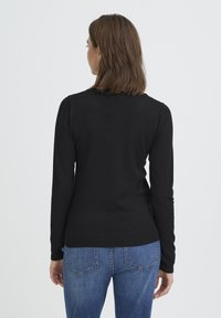 Must pikkade varrukatega kampsun, valmistatud siledast kudumkangast, tihedalt istuva lõikega. Omab ümarat kaelust ja soonikutega ääreosa, sobitatud siniste teksadega.