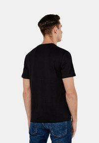 T-shirt nera in cotone con maniche corte, collo rotondo e forma aderente, vista da dietro. Texture liscia e design minimalista.