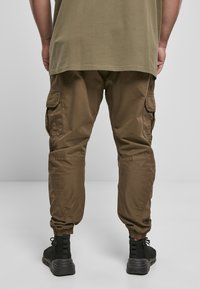 Brune cargo bukser med elastiske manchetter, med sidelommer. Båret med en løs olivenfarvet t-shirt og sorte kondosko.