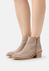 Beige rei'it sandaler med perforering og lav, stablet hæl, prydet med en glat tekstur og minimalistisk design, omkranset af en kontrastkant.