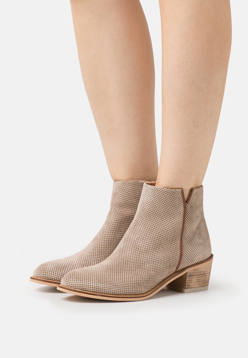 Beige rei'it sandaler med perforering og lav, stablet hæl, prydet med en glat tekstur og minimalistisk design, omkranset af en kontrastkant.