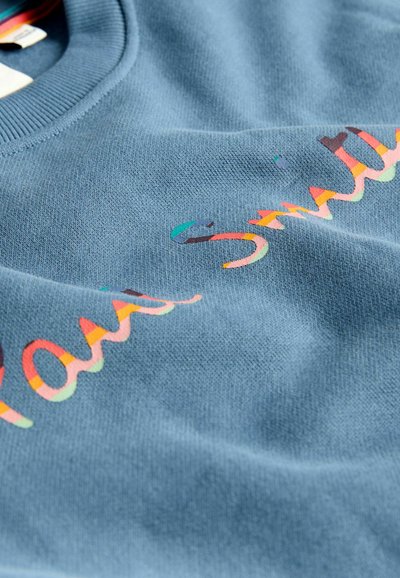 Niebieska bluza z miękkiej tkaniny i ściągaczem przy kołnierzu. Na przodzie znajduje się napis "Paul Smith" w wielokolorowej, stylizowanej czcionce.