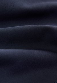 Marineblauer Stoff mit glatter Textur und dezentem Glanz, versehen mit diagonalen Rippenmustern. Das Material wirkt leicht und fällt weich.