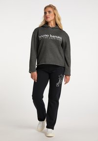 Kulørt hoodie med frontprint, parret med sorte sweatpants med hvid tekst og rhinsten-accenter, iført hvide sneakers.