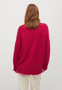 Pull rose surdimensionné en tissu tricoté duveteux, avec un ourlet et des poignets côtelés, une silhouette ample et des épaules tombantes.