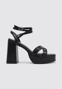 Sandalias de plataforma negras con textura de cocodrilo brillante, tacón ancho y correas en forma de cruz en el tobillo. Detalle de cierre con hebilla ajustable.