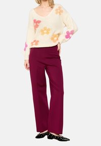 Pletený svetr v krémové barvě s barevnými květinovými vzory, kombinovaný s kalhotami s vysokým pasem a širokými nohavicemi v bordó barvě a černými balerínami s dírkovanými detaily.