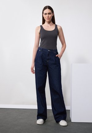 Mørkeblå vide jeans med høj talje, frontlommer og knaplukning, sammen med en tætsiddende grå tanktop og hvide sneakers.