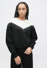 Czarna bluza z białym wzorem w kształcie szewrona przy dekolcie, ozdobiona frędzlami. Długie rękawy i prążkowane mankiety dopełniają całość.