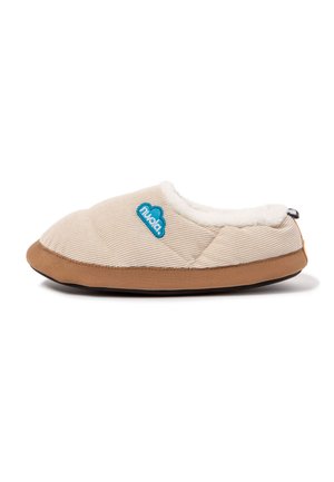 Zapatilla beige acolchada con suela marrón, forro interior de felpa blanca y parche azul con logo en el lateral, diseñada para la comodidad en interiores.
